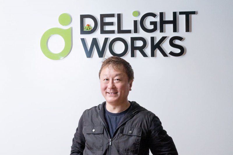 Yoshinori Ono con l'inseparabile Blanka davanti al logo di Delight Works.