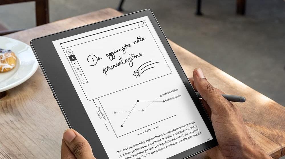 Un Kindle Scribe tenuto in mano davanti a un tavolo