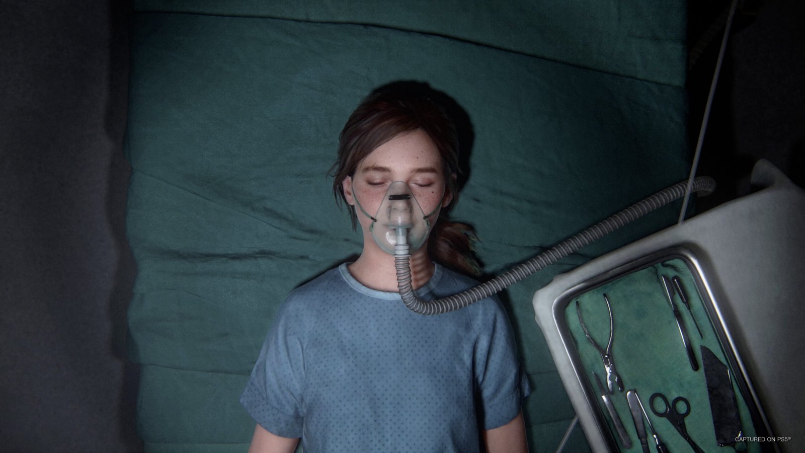 Ellie di The Last of Us Parte 1 stesa su un letto d'ospedale con una maschera dell'ossigeno sul volto